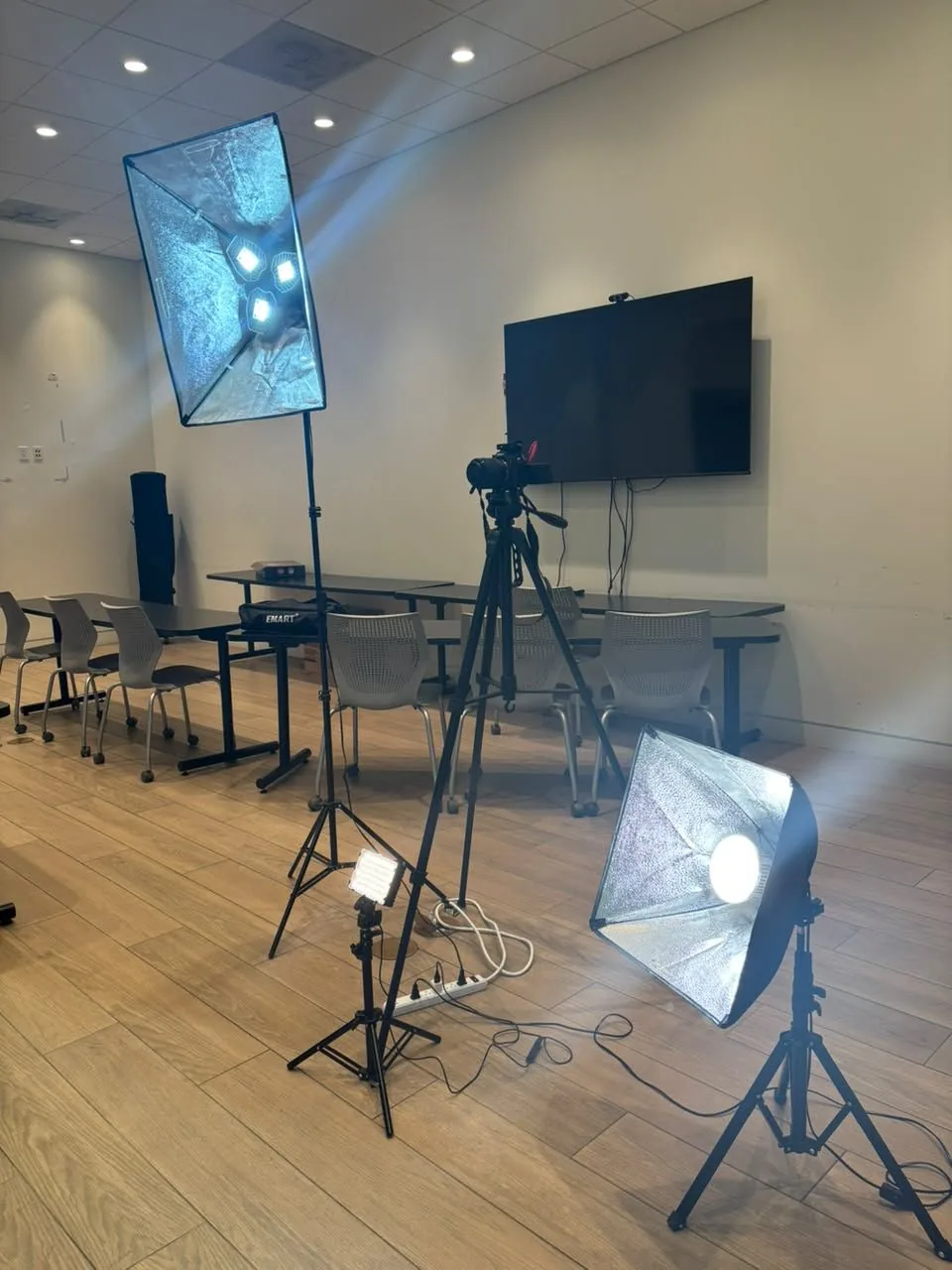 Two softbox lights, a small LED panel and a camera on a tripod set up in a meeting room for an onsite video shoot